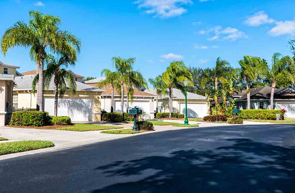 Image at the bottom of page of a typical south Florida town home neighborhood. Several home lots with lush landscaping and palm trees accenting each property. 